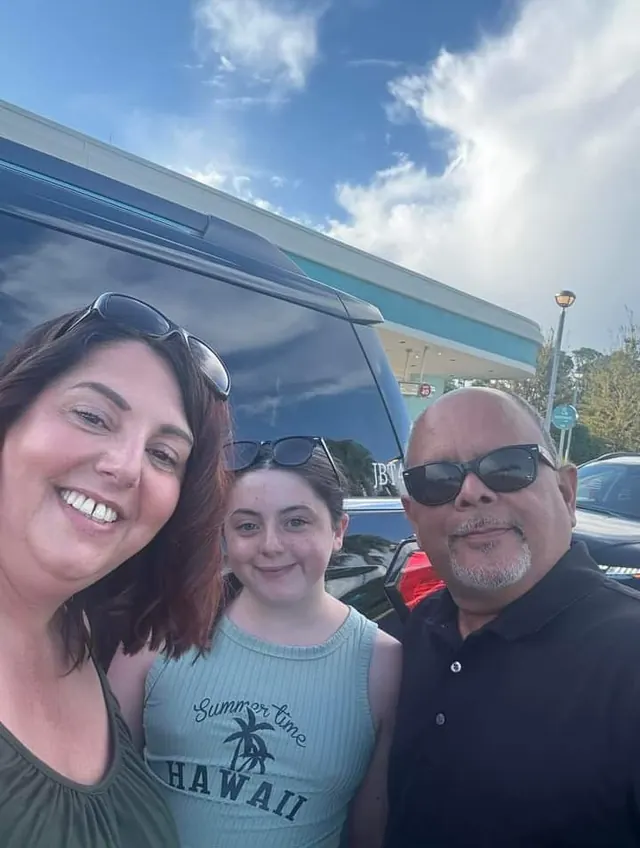 A mother and daughter with Pedro beside a JOB SUV after a theme park night