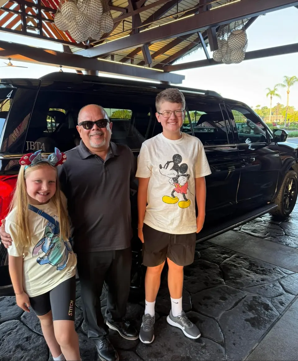Pedro with two young riders beside a JOB SUV at a resort entrance