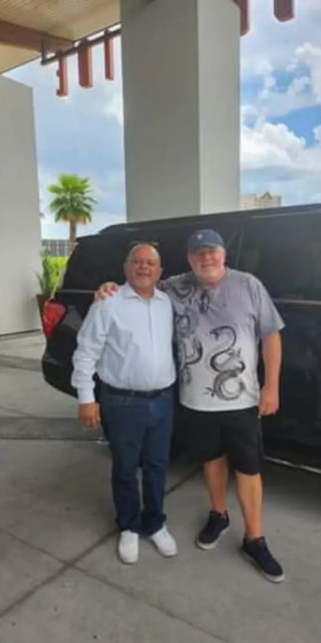 Pedro with a longtime rider beside a JOB SUV at a hotel entrance